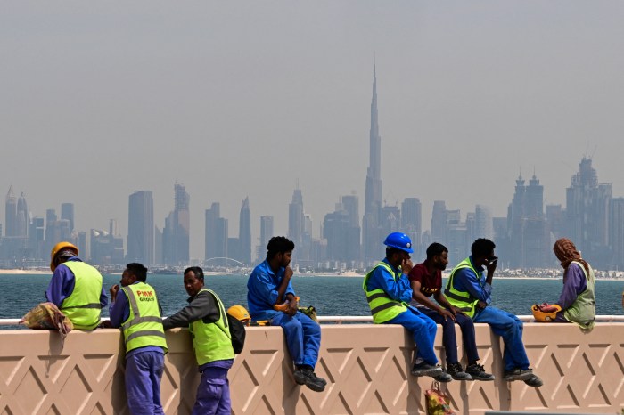 Workers resting on a wall with the Dubai skyline and Burj Khalifa in the background.